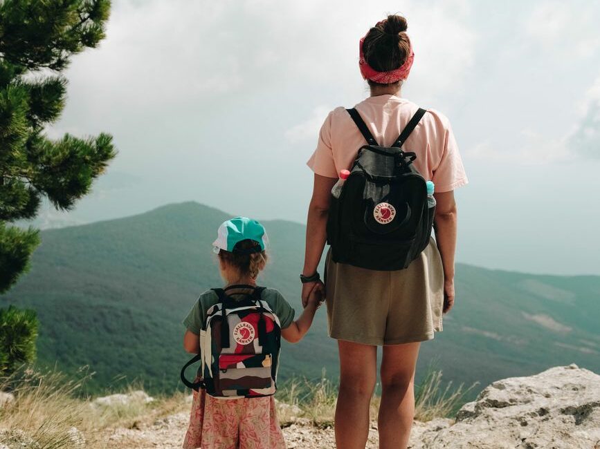 woman and a girl with backpacks standing on a mountain cliff
